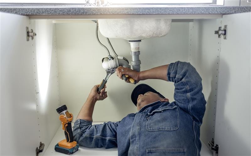 Plumber repairing pipes beneath a bathroom sink in Battleground