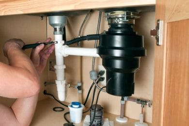 Plumber repairing a garbage disposal beneath a kitchen sink in Battleground