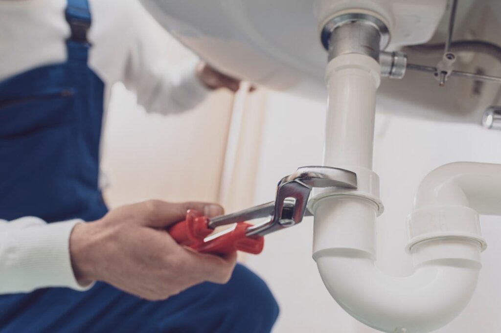 Plumber repairing a white drain pipe beneath a sink in Battleground
