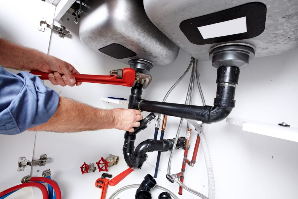 Plumber repairing drain pipes beneath a kitchen sink in Battleground